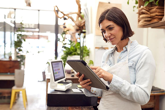 Shop owner managing orders on a tablet beside a point-of-sale terminal